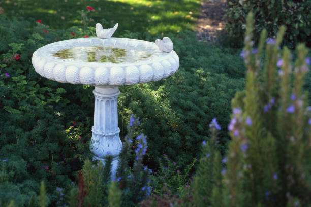 White decorative garden bird bath with bird statues amidst lush greenery.