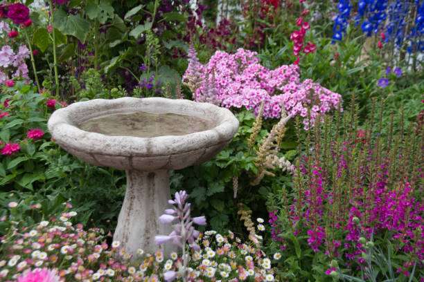 Classic concrete bird bath surrounded by an abundance of colorful pink, purple, and red garden flowers.